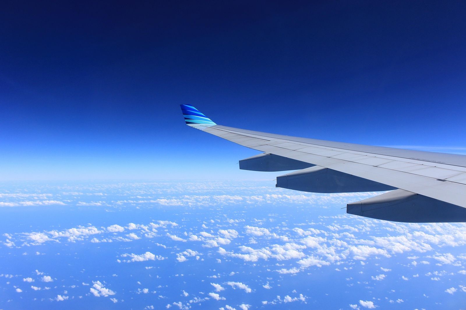 Aircraft wing above the clouds on approach to an international airport, where travellers collect their rental car.
